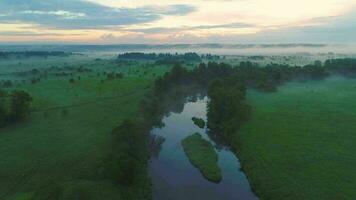 Flying over river, green field and trees in morning haze. Aerial view. Warm tint. video