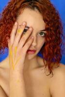 redhead curly woman hands in yellow paint looks at the camera photo