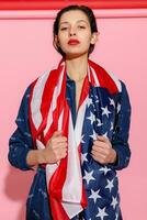 Portrait female athlete wrapped in American Flag against pink background photo