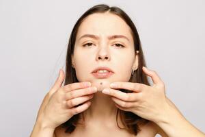 Portrait of young attractive woman touching her face and looking for acne photo