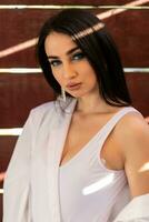 Glamorous young woman in white shirt posing near a wall photo