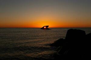 The sunken ship of Cape May New Jersey during sunset. The sun lining up perfectly with hull to look like a glowing eye. The sky has beautiful colors of orange almost like it is on fire. photo