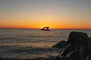 The sunken ship of Cape May New Jersey during sunset. The sun lining up perfectly with hull to look like a glowing eye. The sky has beautiful colors of orange almost like it is on fire. photo