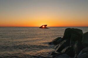 The sunken ship of Cape May New Jersey during sunset. The sun lining up perfectly with hull to look like a glowing eye. The sky has beautiful colors of orange almost like it is on fire. photo