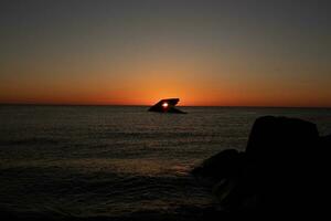 The sunken ship of Cape May New Jersey during sunset. The sun lining up perfectly with hull to look like a glowing eye. The sky has beautiful colors of orange almost like it is on fire. photo