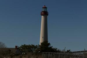 This is Cape May point lighthouse seen from the beach. The tall white structure with red metal serves as a beacon of safety. photo