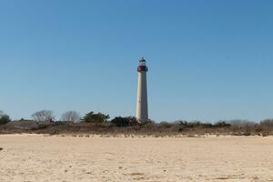 This is Cape May point lighthouse seen from the beach. The tall white structure with red metal serves as a beacon of safety. photo