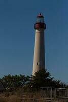 This is Cape May point lighthouse seen from the beach. The tall white structure with red metal serves as a beacon of safety. photo