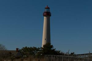 This is Cape May point lighthouse seen from the beach. The tall white structure with red metal serves as a beacon of safety. photo
