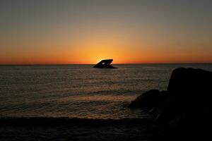 Sunset beach in Cape May New Jersey where you can get a great view of the sun going down across the ocean and the bay. The reflection of the sun on the water with the sunken ship looks so beautiful. photo