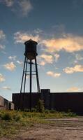 A beautiful water tower is set around an abandoned area. This rusty metal structure stands tall against a blue sky. photo