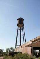 A beautiful water tower is set around an abandoned area. This rusty metal structure stands tall against a blue sky. photo