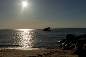 Sunset beach in Cape May New Jersey where you can get a great view of the sun going down across the ocean and the bay. The reflection of the sun on the water with the sunken ship looks so beautiful. photo