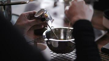 Woman's hand stirs melted wax in a metal ladle with a wooden stick. video