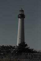 This is Cape May point lighthouse seen from the beach. The tall white structure with red metal serves as a beacon of safety. photo