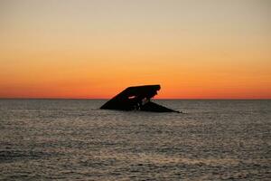 Sunset beach in Cape May New Jersey where you can get a great view of the sun going down across the ocean and the bay. The reflection of the sun on the water with the sunken ship looks so beautiful. photo