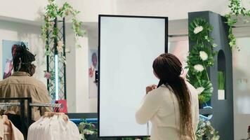 afrikanisch amerikanisch Frau im Mode Boutique mit Attrappe, Lehrmodell, Simulation erweitert Wirklichkeit Bildschirm zu aussehen beim Kleider Optionen zu Versuchen An. Kunde mit LED Kiosk zu visualisieren Outfit Kombinationen im Geschäft Vor Kauf video