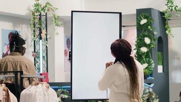 African american woman in fashion boutique using mockup augmented reality screen to look at clothes options to try on. Customer using led kiosk to visualize outfit combinations in store before buying video