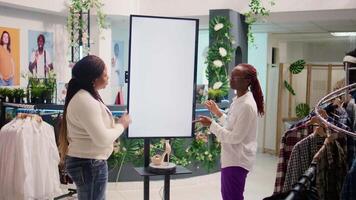 Employee in shopping center fashion boutique using high tech screen to show woman clothes options to try on. Shopkeeper using led panel to help client visualize outfit combinations before buying video