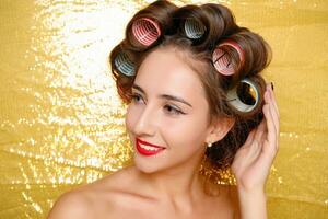 Beautiful girl in hair curlers isolated on gold photo