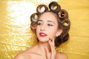 Beautiful girl in hair curlers isolated on gold photo