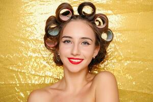 Beautiful girl in hair curlers isolated on gold photo