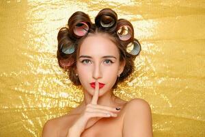 Beautiful girl in hair curlers isolated on gold photo