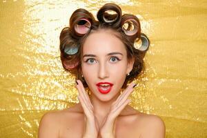 Beautiful girl in hair curlers isolated on gold photo