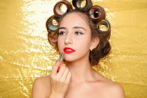 Beautiful girl in hair curlers isolated on gold photo