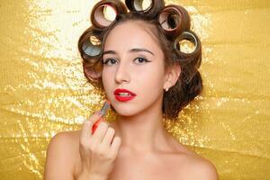 Beautiful girl in hair curlers isolated on gold photo