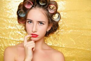 Beautiful girl in hair curlers isolated on gold photo