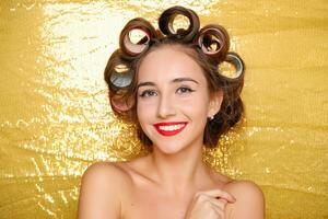 Beautiful girl in hair curlers isolated on gold photo