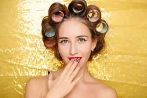 Beautiful girl in hair curlers isolated on gold photo