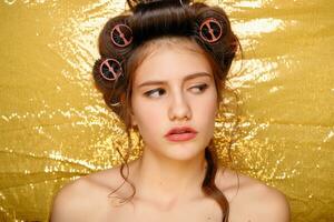 Beautiful girl in hair curlers isolated on gold photo