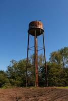 un hermosa agua torre es conjunto alrededor un abandonado área. esta oxidado metal estructura soportes alto en contra un azul cielo. foto