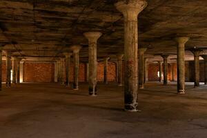 This abandoned warehouse sat completely empty. All of the cement pillars supporting the roof from falling in. The roof looks to have black mold on it. The tan colors all around void from life. photo