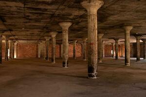 This abandoned warehouse sat completely empty. All of the cement pillars supporting the roof from falling in. The roof looks to have black mold on it. The tan colors all around void from life. photo