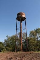 un hermosa agua torre es conjunto alrededor un abandonado área. esta oxidado metal estructura soportes alto en contra un azul cielo. foto