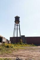 un hermosa agua torre es conjunto alrededor un abandonado área. esta oxidado metal estructura soportes alto en contra un azul cielo. foto
