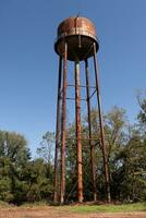 un hermosa agua torre es conjunto alrededor un abandonado área. esta oxidado metal estructura soportes alto en contra un azul cielo. foto