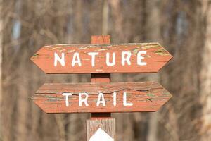 This sign in the woods marks the area of the trail. Helping to keep hikers from getting them lost and leading the way. The brown paint looks worn and chipping. The white letters standing out. photo