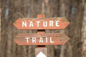 This sign in the woods marks the area of the trail. Helping to keep hikers from getting them lost and leading the way. The brown paint looks worn and chipping. The white letters standing out. photo