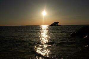 Sunset beach in Cape May New Jersey where you can get a great view of the sun going down across the ocean and the bay. The reflection of the sun on the water with the sunken ship looks so beautiful. photo