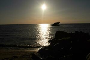 Sunset beach in Cape May New Jersey where you can get a great view of the sun going down across the ocean and the bay. The reflection of the sun on the water with the sunken ship looks so beautiful. photo