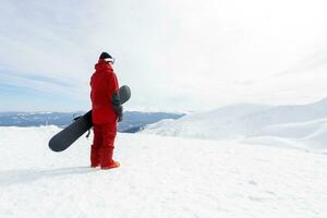 Snowboarder stands on backcountry slope and holds snowboard. photo