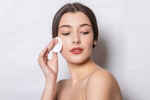 girl cleanses the skin on her face with a cotton ball photo