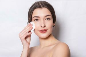 girl cleanses the skin on her face with a cotton ball photo