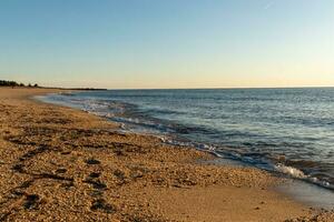 Pretty look of this beach as the waves came in to the shore. The water looking calm and the sand a golden brown. The beautiful sky with no clouds in site makes this look like a beautiful summer day. photo