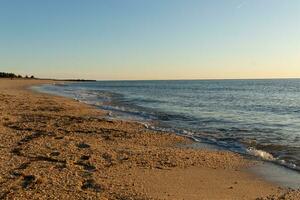 Pretty look of this beach as the waves came in to the shore. The water looking calm and the sand a golden brown. The beautiful sky with no clouds in site makes this look like a beautiful summer day. photo