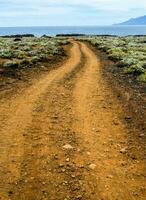 a dirt road leads to the ocean in the middle of a desert photo